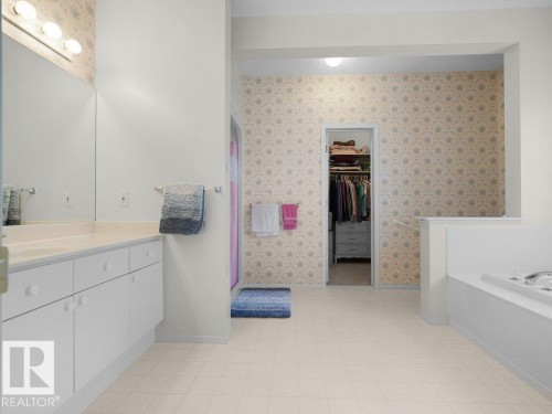 Located on the main floor. Expansive bathroom featuring a dual-sink vanity with white cabinetry, a built-in bathtub, and tiled flooring - 156 Phillips Row Nw, Edmonton, AB 