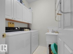 Located on the main floor. White cabinetry with arch details, utility sink with tile backsplash, and light-toned flooring - 