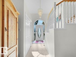 Arched front door with decorative glass inserts, chandelier lighting, tiled flooring, wood-finish staircase handrail, and white paneled bi-fold doors - 
