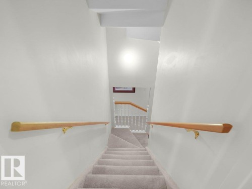 Carpeted staircase with light-toned wood-finish handrails and white balusters - 156 Phillips Row Nw, Edmonton, AB 
