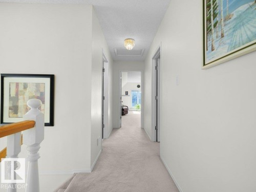 Carpeted hallway with white walls, multiple doorways, and a flush mount ceiling light - 156 Phillips Row Nw, Edmonton, AB 