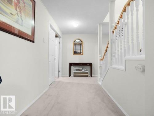 Wall-to-wall carpeting, staircase with wood handrail, white balusters, and a built-in closet with bifold doors - 156 Phillips Row Nw, Edmonton, AB 