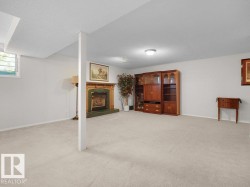 Expansive carpeted room featuring a fireplace with a wood mantel and green surround, a built-in wood-finish cabinet system, and a window with horizontal blinds - 