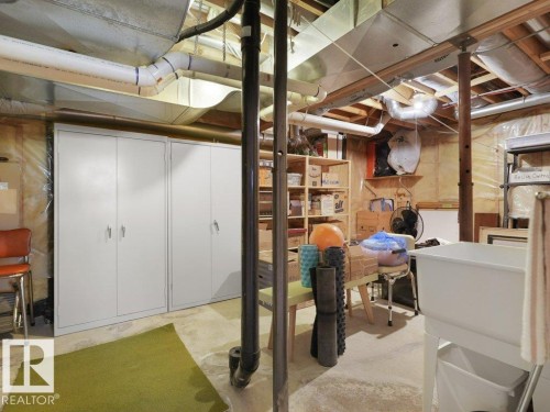 Unfinished basement with exposed ceiling joists and ductwork, featuring concrete flooring, built-in storage cabinets, and a utility sink - 156 Phillips Row Nw, Edmonton, AB 