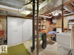 Unfinished basement with exposed ceiling joists and ductwork, featuring concrete flooring, built-in storage cabinets, and a utility sink - 