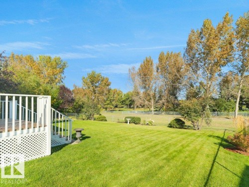 Expansive backyard featuring a manicured lawn, mature trees, and a white deck with lattice skirting and railings - 156 Phillips Row Nw, Edmonton, AB 