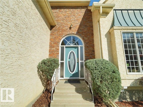 Arched entry door with decorative glass, flanked by natural stone veneer and textured stucco - 156 Phillips Row Nw, Edmonton, AB 