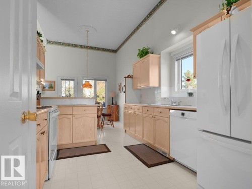 Kitchen featuring light wood-finish cabinetry, white appliances, and a tiled backsplash - 156 Phillips Row Nw, Edmonton, AB 