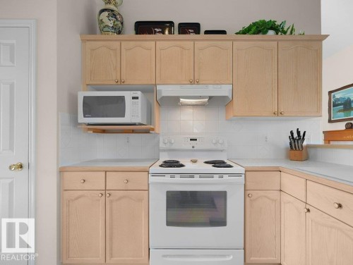 Light wood-finish cabinetry, white tile backsplash, light-toned countertops, built-in microwave, and electric range - 156 Phillips Row Nw, Edmonton, AB 