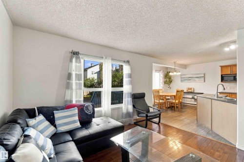 Spacious open-concept living area featuring wood-finish flooring, ample natural light from multiple windows, and a dedicated dining space with an overhead chandelier - 3524 Mclean Crescent Sw, Edmonton, AB 