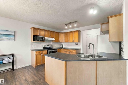 Kitchen featuring wood-finish cabinetry, dark countertops, stainless steel appliances, and wood-finish flooring - 3524 Mclean Crescent Sw, Edmonton, AB 