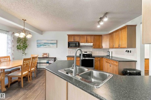 Kitchen and dining area featuring wood-finish cabinetry, stainless steel appliances, a double basin sink, and wood-finish flooring - 3524 Mclean Crescent Sw, Edmonton, AB 