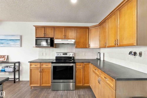Kitchen featuring wood-finish cabinetry, dark countertops, white tile backsplash, and wood-finish flooring - 3524 Mclean Crescent Sw, Edmonton, AB 