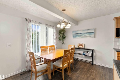 Dining area featuring wood-finish flooring, a contemporary chandelier, and a window with vertical blinds - 3524 Mclean Crescent Sw, Edmonton, AB 