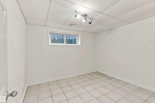 Recessed window with blinds, white tile flooring, track lighting, drop ceiling, and white painted walls - 3524 Mclean Crescent Sw, Edmonton, AB 