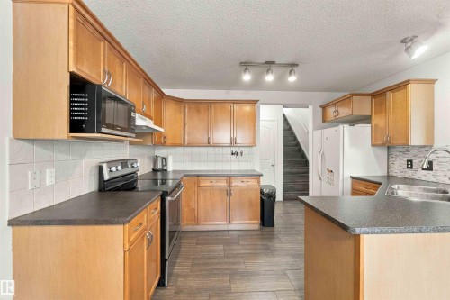 Expansive kitchen featuring light wood cabinetry, dark countertops, built-in stainless steel appliances, and wood-finish flooring - 3524 Mclean Crescent Sw, Edmonton, AB 