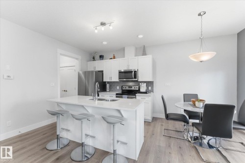 Kitchen featuring white cabinetry, stainless steel appliances, a grey subway tile backsplash, a kitchen island with seating, and wood-finish flooring - #15 4835 Wright Dr Sw, Edmonton, AB 