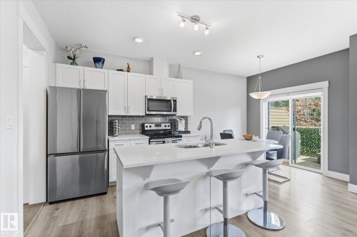 Kitchen featuring stainless steel appliances, white cabinetry, a large island with a sink, quartz countertops, and wood-finish flooring - #15 4835 Wright Dr Sw, Edmonton, AB 