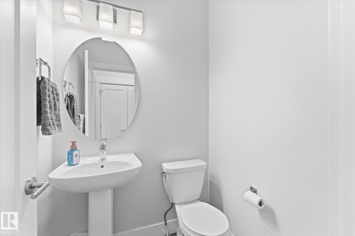 Pedestal sink, wall-mounted mirror, modern overhead lighting, white toilet, and chrome fixtures - #15 4835 Wright Dr Sw, Edmonton, AB 