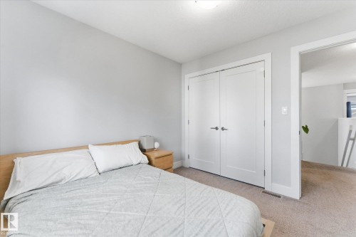 Soft gray walls with white trim, light-colored wood-finish headboard, and dual white paneled doors - #15 4835 Wright Dr Sw, Edmonton, AB 