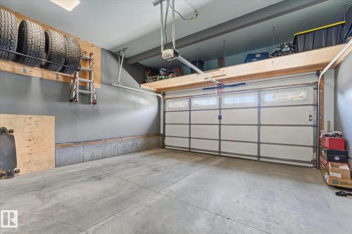 Concrete flooring, overhead garage door with window panels, high ceiling, built-in overhead storage, and wall-mounted tire rack - #15 4835 Wright Dr Sw, Edmonton, AB 