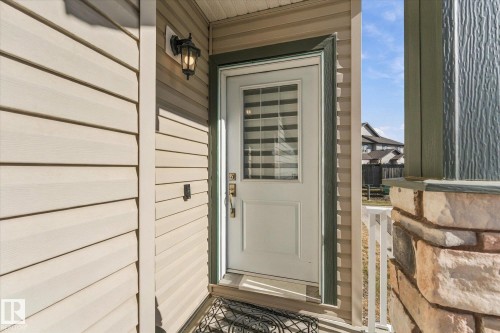 White entry door with integrated blinds, exterior wall lantern, and stone-clad porch column - #15 4835 Wright Dr Sw, Edmonton, AB 