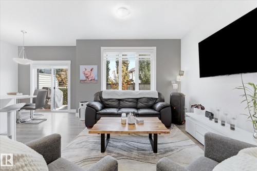 Open-concept living area with light wood-finish flooring, white walls, and a grey accent wall - #15 4835 Wright Dr Sw, Edmonton, AB 