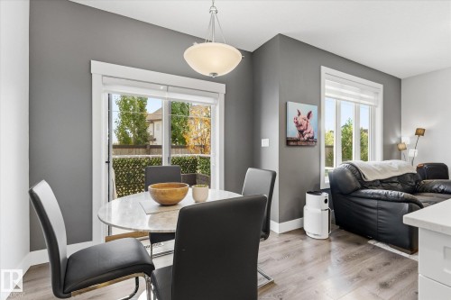 Sliding glass door, pendant light fixture, wood-finish flooring, white trim, and a window with a roller shade - #15 4835 Wright Dr Sw, Edmonton, AB 