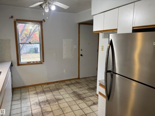 White upper cabinetry, stainless steel refrigerator, and a window with wood trim - 7623 130 Avenue Nw, Edmonton, AB 