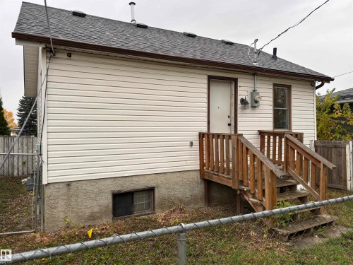 White siding exterior, shingle roof, brown gutters, wood deck with railings, and a basement window - 7623 130 Avenue Nw, Edmonton, AB 
