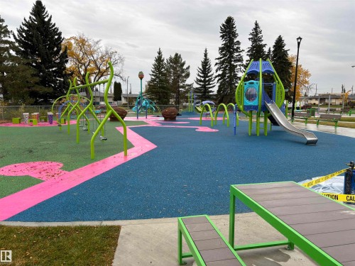 Community park featuring a play structure with a slide, multiple swing sets, and a blue and green soft-fall surface - 7623 130 Avenue Nw, Edmonton, AB 