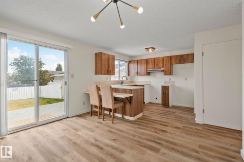 Wood-finish flooring throughout, kitchen with wood cabinetry and light countertops, modern ceiling light fixture, sliding glass door, and a private fenced yard with a patio - 14411 23 Street Nw, Edmonton, AB 