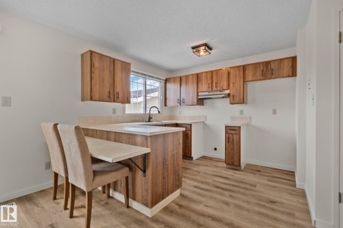 Kitchen featuring wood-finish cabinetry, light-toned countertops, a stainless steel range hood, and wood-finish flooring - 14411 23 Street Nw, Edmonton, AB 