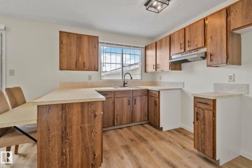 Wood-finish flooring, wood-finish cabinetry, light-toned countertops, window with security bars, and a black faucet - 14411 23 Street Nw, Edmonton, AB 