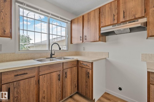 Wood-finish cabinetry with matte black hardware, dual stainless steel sink, black gooseneck faucet, light-toned countertops, and a stainless steel range hood - 14411 23 Street Nw, Edmonton, AB 