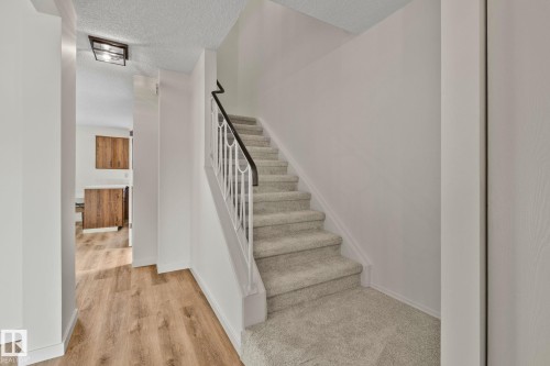 Carpeted staircase with an ornamental metal railing and dark wood-finish handrail, complemented by wood-finish flooring in the foreground - 14411 23 Street Nw, Edmonton, AB 