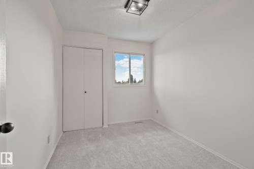 Neutral tone walls, light gray carpet, window with exterior scenery, bi-fold closet, and ceiling-mounted light fixture - 14411 23 Street Nw, Edmonton, AB 