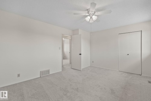 Neutral-toned carpet flooring, a ceiling fan with integrated lighting, and two white bi-fold closet doors - 14411 23 Street Nw, Edmonton, AB 