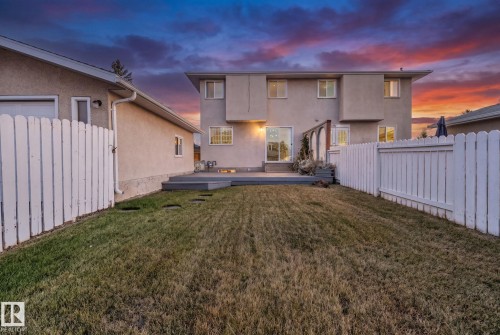 Expansive backyard with a level lawn, white picket fencing, and a built-in outdoor deck - 14411 23 Street Nw, Edmonton, AB 