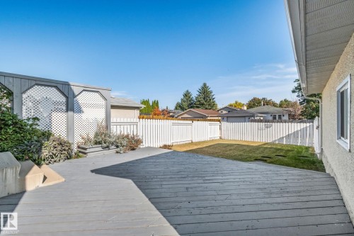 Expansive wooden deck with a built-in planter, surrounded by a white privacy fence and a patch of grass - 14411 23 Street Nw, Edmonton, AB 