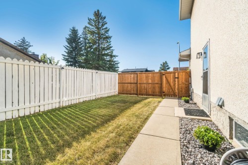 Manicured lawn, white picket fencing, wood fencing, concrete pathway, and exterior wall lighting - 14411 23 Street Nw, Edmonton, AB 