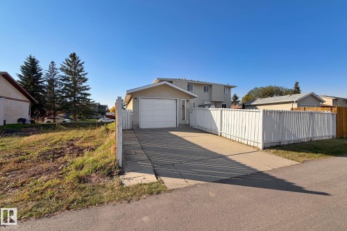 Detached garage with a white panel door, concrete driveway, and white picket fence - 14411 23 Street Nw, Edmonton, AB 