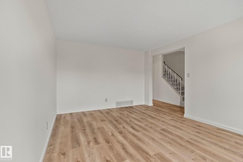 Light-toned wood-finish flooring, white painted walls, and a staircase with a metal railing - 14411 23 Street Nw, Edmonton, AB 