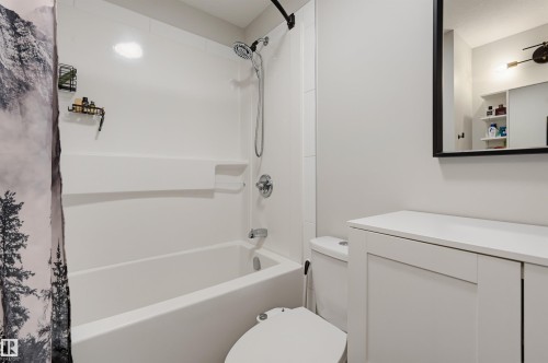 White bathtub with an integrated shower, chrome fixtures, a white vanity with recessed panel cabinet doors, a white countertop, and a framed mirror - 9020 152 Street Nw, Edmonton, AB 