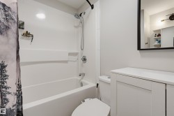 White bathtub with an integrated shower, chrome fixtures, a white vanity with recessed panel cabinet doors, a white countertop, and a framed mirror - 