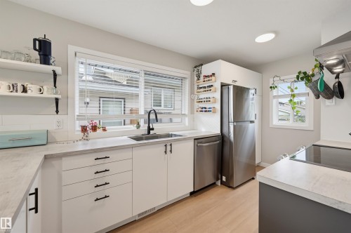 Modern kitchen featuring light wood-finish flooring, white cabinetry with black hardware, stainless steel appliances, and built-in open shelving - 9020 152 Street Nw, Edmonton, AB 