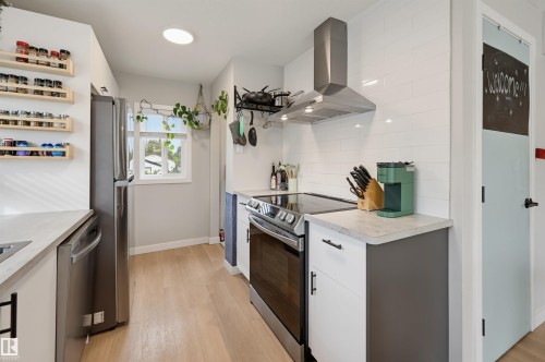 Modern kitchen featuring wood-finish flooring, stainless steel appliances, white subway tile backsplash, and light-toned countertops - 9020 152 Street Nw, Edmonton, AB 