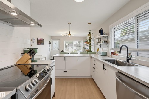 White cabinetry with matte black hardware, stainless steel appliances, light wood-finish flooring, white subway tile backsplash, and a stainless steel sink with a matte black gooseneck faucet - 9020 152 Street Nw, Edmonton, AB 
