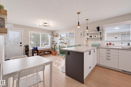 Open-concept living space with light wood-finish flooring, white cabinetry, and a kitchen island with pendant lighting - 9020 152 Street Nw, Edmonton, AB 