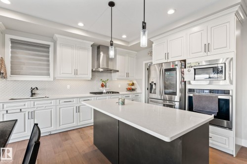 White shaker cabinetry, stainless steel appliances, central island with solid surface countertop, wood-finish flooring, and pendant lighting - 824 34 Ave Nw, Edmonton, AB 